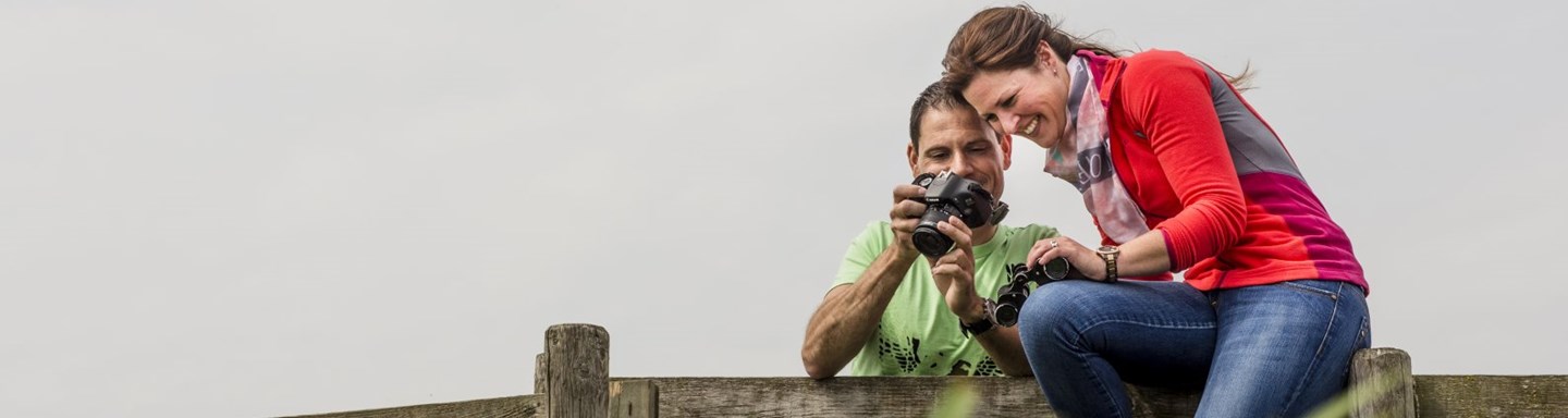 wandelaars bekijken hun foto's zittend op een landhek aan de Diefdijk